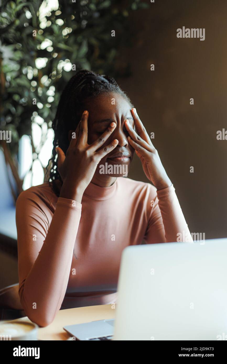 Jeune femme afro-américaine malheureuse avec des dreadlocks pleurant couvrant les yeux avec les mains dans la maison de café de près. Dépression fille noire souffrance, dépairé Banque D'Images