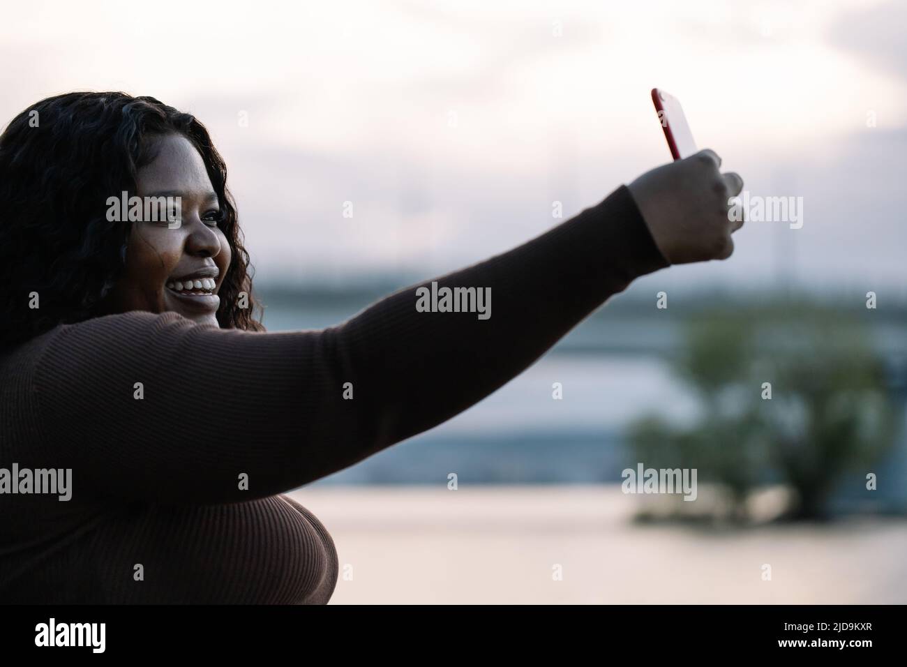 Jolie femme interraciale souriante en robe prendre selfie, appel vidéo, photo smartphone, poser contre le ciel. Acceptation Banque D'Images
