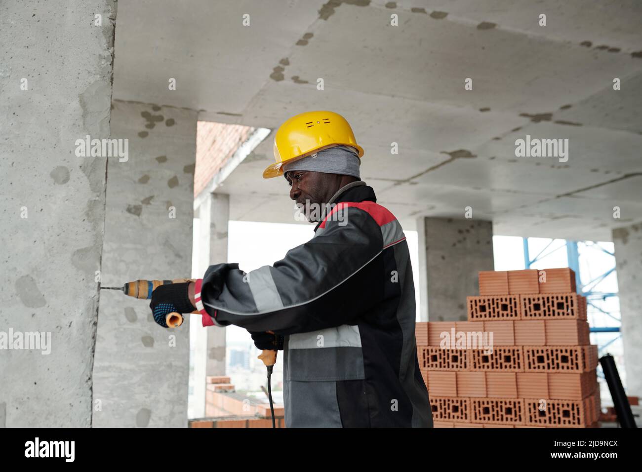 Constructeur américain africain mature de vêtements de travail et de casque  à l'aide de foreuses électriques tout en forant un mur de béton épais de  construction non finie Photo Stock - Alamy