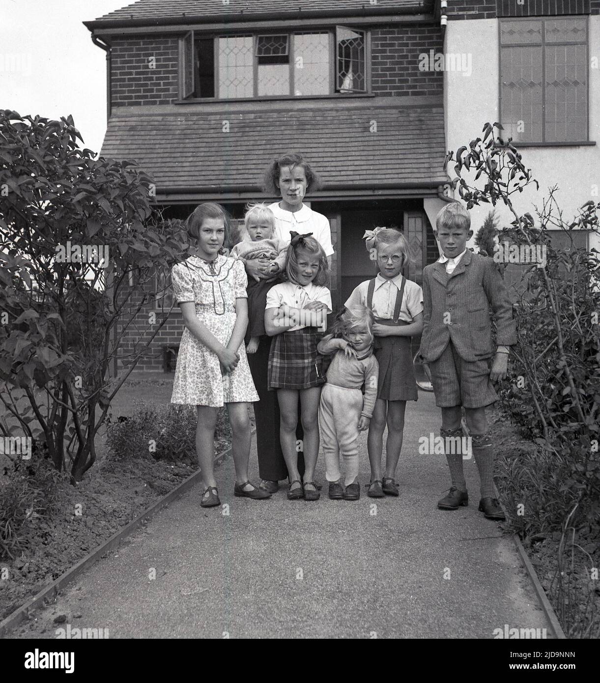 1940s, historique, une mère debout avec ses enfants pour une photo, sur le chemin d'entrée de leur maison sur Woodford Rd, près du village de Bramhall, une banlieue prospère de Stockport, Cheadle, Angleterre, Royaume-Uni. Banque D'Images