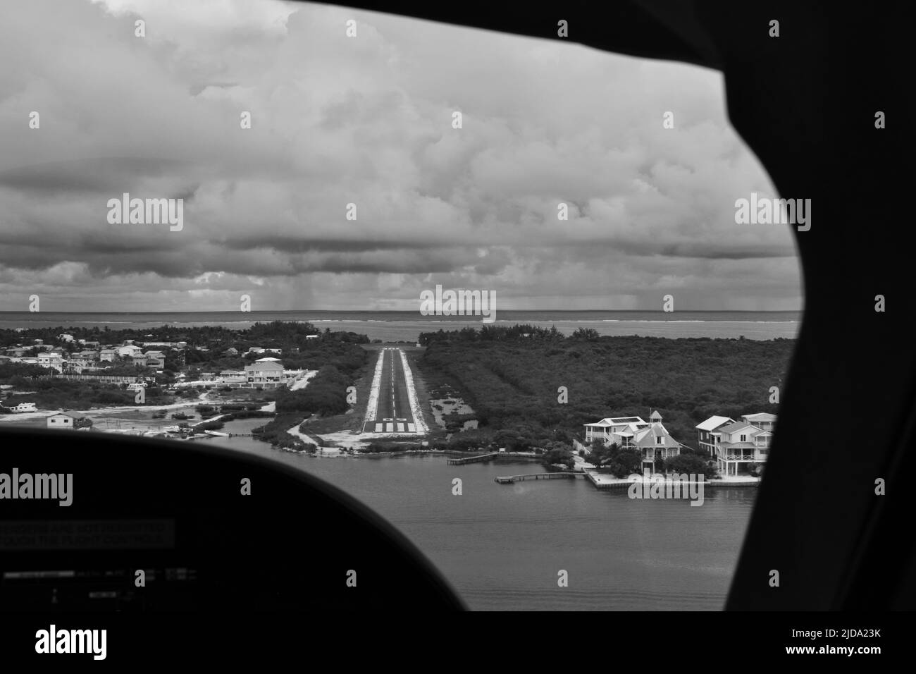 Un coup de feu noir et blanc de la piste de l'aéroport de Caye Caulker vu du poste de pilotage par une journée nuageux. Banque D'Images