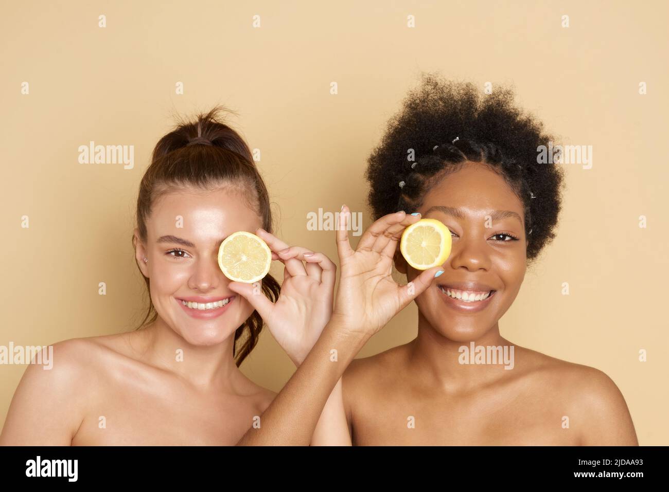 Cercles d'agrumes colorés près du visage de femmes multiraciales gaies souriant et tenant des agrumes frais près des yeux tout en représentant la vitamine C ben Banque D'Images