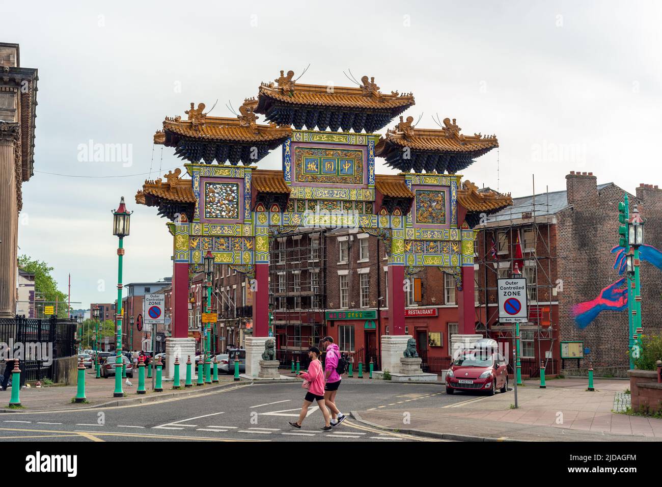 Deux personnes passant devant l'arcade chinoise, la porte ou le paifang à l'entrée du quartier chinois de Liverpool sur Nelson Street. Angleterre, Royaume-Uni Banque D'Images