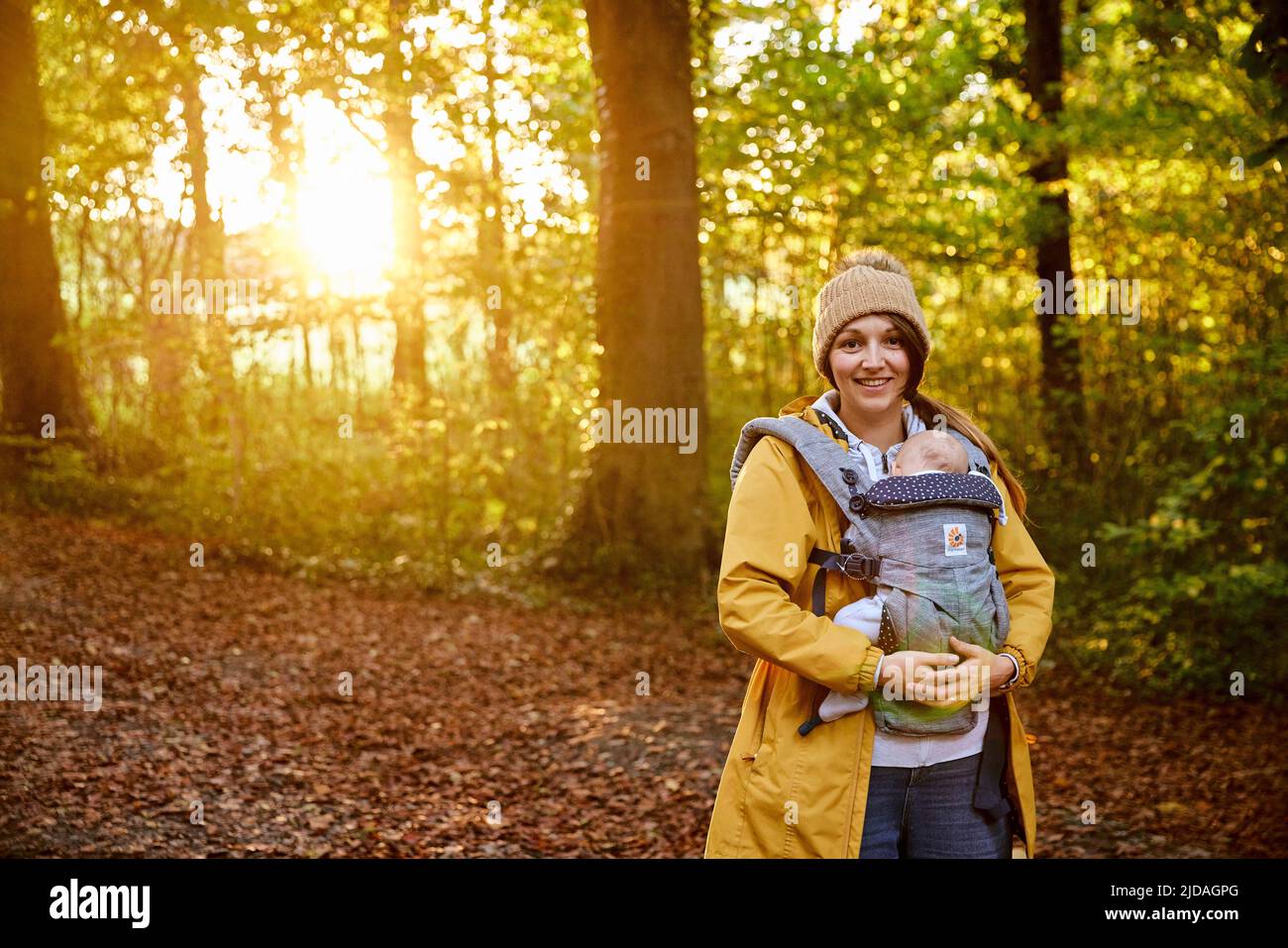 Portrait d'une mère souriante portant son bébé endormi dans un porte-bébé dans les bois, automne Banque D'Images