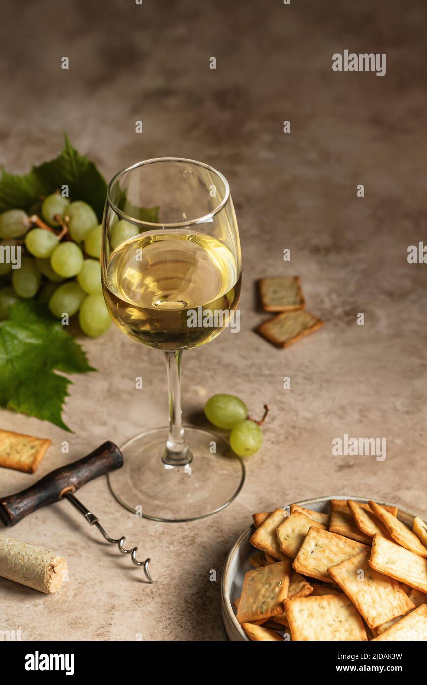 Un verre de vin blanc sur fond texturé avec des tire-bouchon, des raisins et des craquelins. Espace de texte. Décor rustique pour la carte des vins. Orientation verticale. Hai Banque D'Images