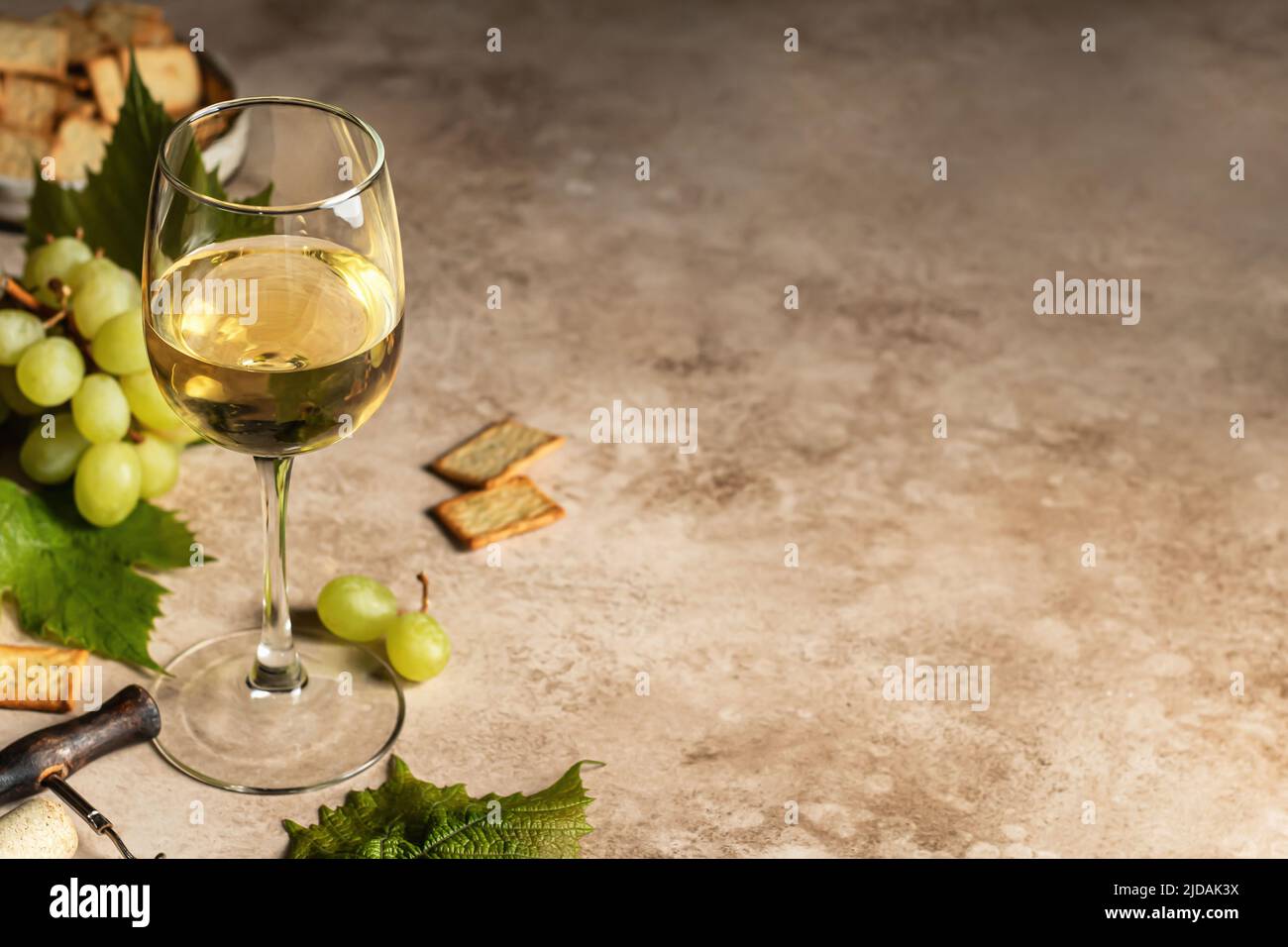 Un verre de vin blanc sur fond texturé avec des tire-bouchon, des raisins et des craquelins. Espace de texte. Décor rustique pour la carte des vins. Orientation de l'horisontal Banque D'Images