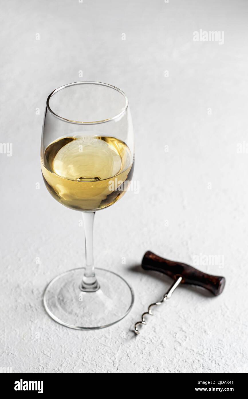 Un verre de vin blanc sur fond blanc texturé avec tire-bouchon. Copier l'espace. Orientation verticale Banque D'Images
