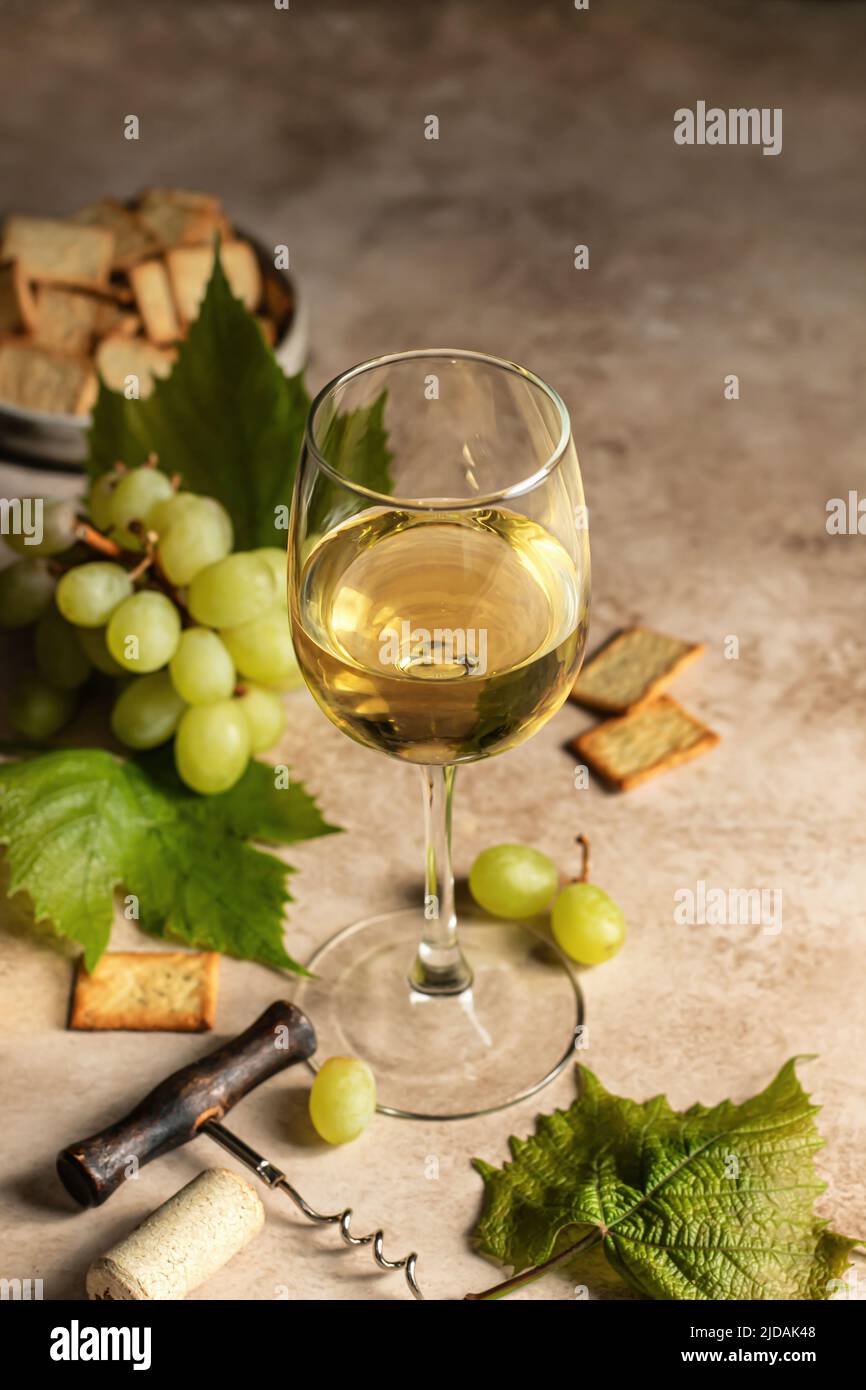 Verre à vin blanc sur fond brun texturé avec tire-bouchon, raisins et craquelins. Espace de texte. Décor rustique pour la carte des vins. Orientation verticale Banque D'Images