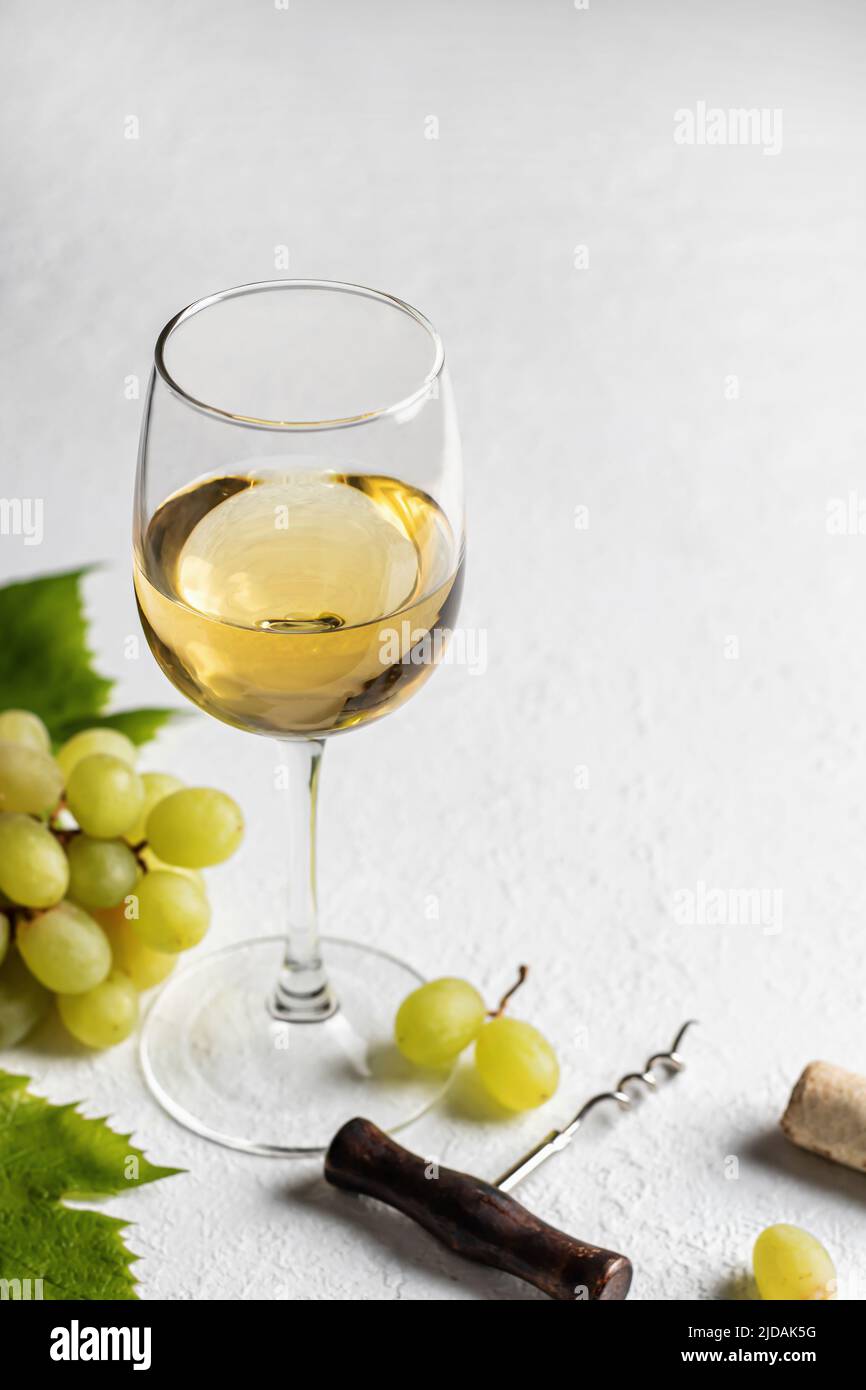 Un verre de vin blanc sur fond blanc texturé avec un tire-bouchon et des raisins avec un espace de texte. Décor rustique pour la carte des vins. Orientation verticale Banque D'Images