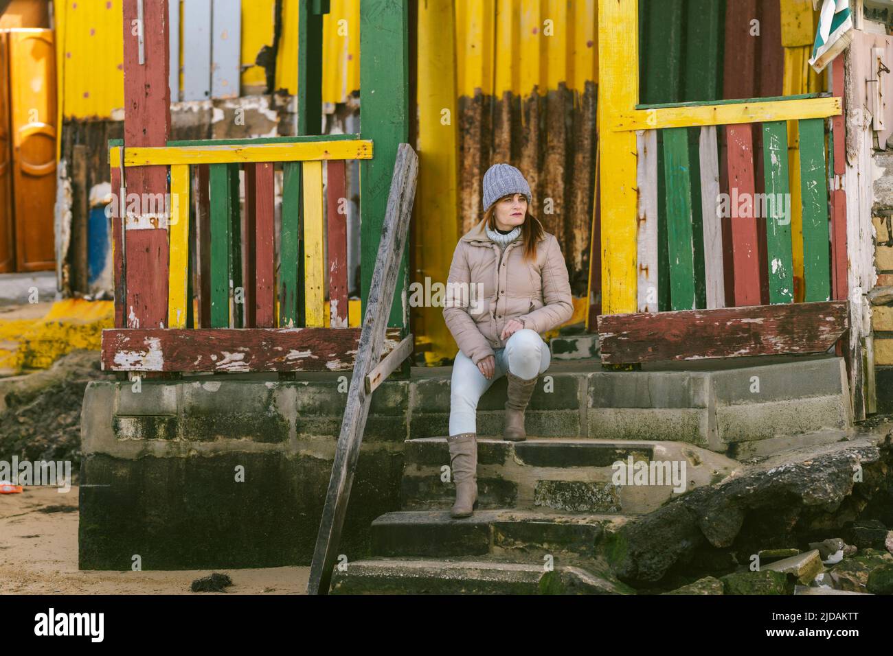 femme en vêtements d'hiver assise sur les marches d'une maison colorée près de la mer Banque D'Images