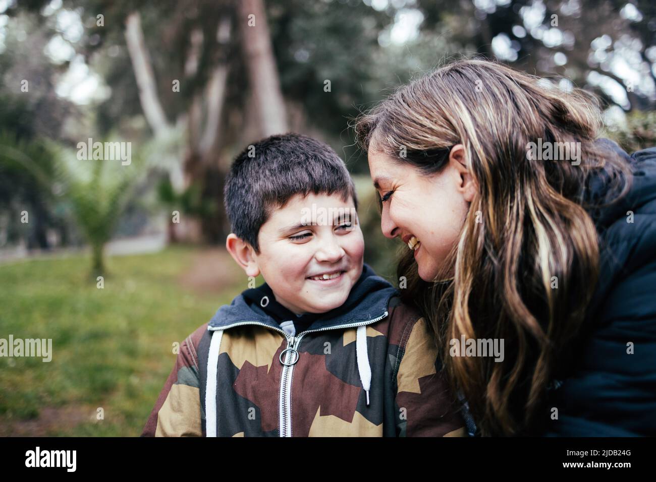 Jeune mère latine blonde embrassant et riant avec son jeune fils dans le parc. Famille monoparentale Banque D'Images