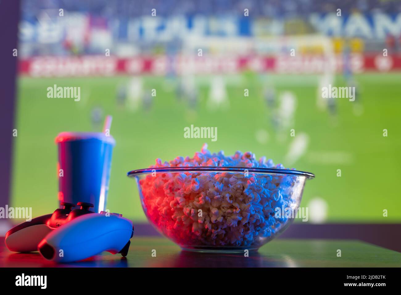 Pop-corn dans un bol en verre, une boisson dans un verre en plastique et  une manette de jeu sur un fond sportif. Jeux vidéo, esports, football,  football américain. Jeu en ligne Photo