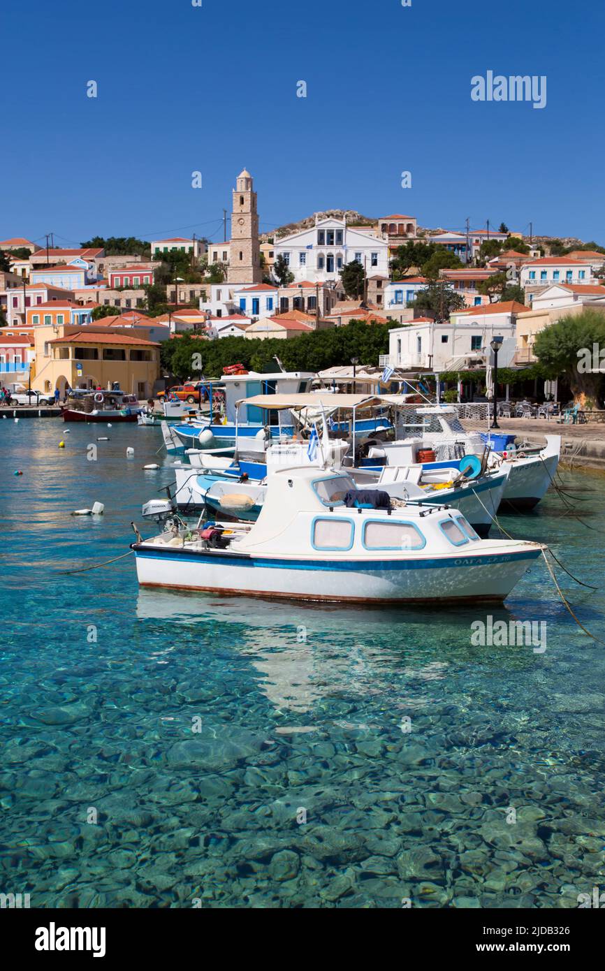 Gros plan de bateaux de pêche amarrés au bord de l'eau dans le port d'Emborio avec des bâtiments traditionnels et la tour de l'horloge dans le centre-ville sur Halki (CH.. Banque D'Images