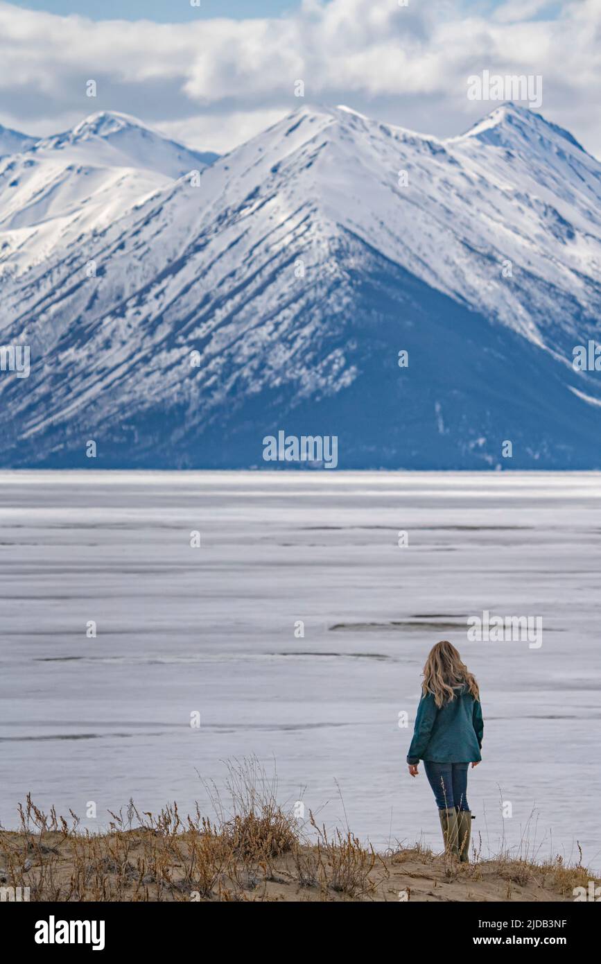 Vue prise de derrière une femme debout sur les dunes de sable et vue sur le lac Bennett gelé et les montagnes enneigées autour de la voiture... Banque D'Images