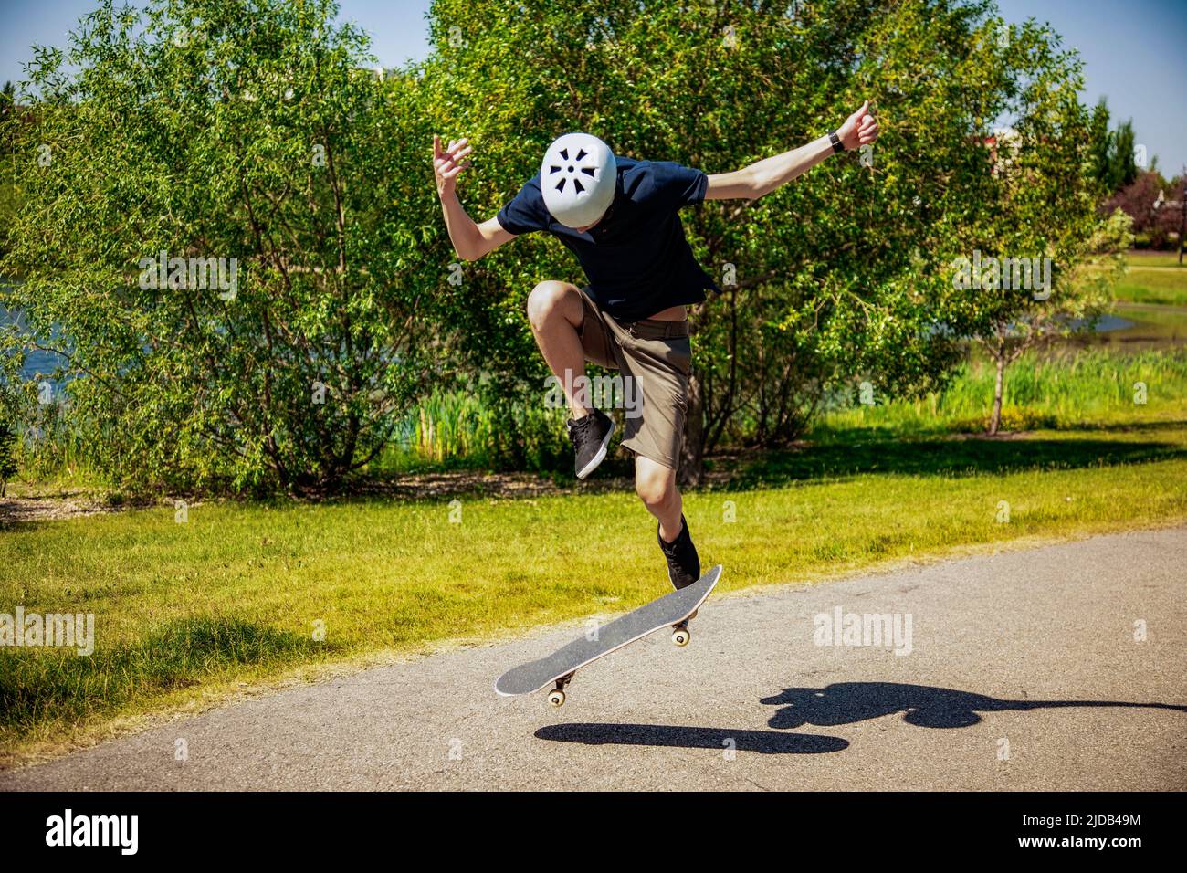 Jeune homme sur un sentier de parc avec un skateboard faisant un tour de bascule; Edmonton, Alberta, Canada Banque D'Images