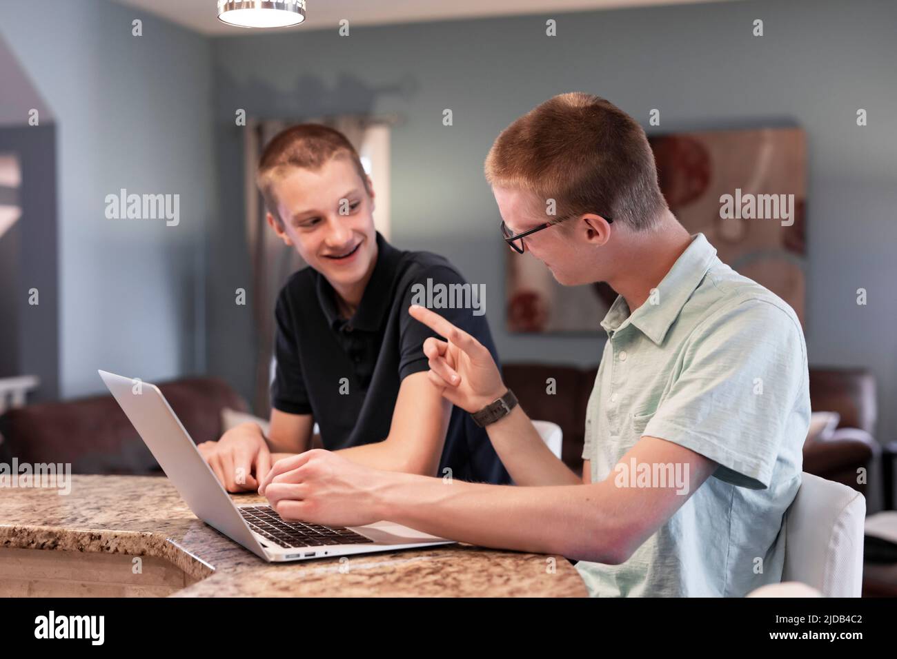 Le jeune homme utilise un ordinateur portable à la maison, son frère l'aidant; Edmonton, Alberta, Canada Banque D'Images