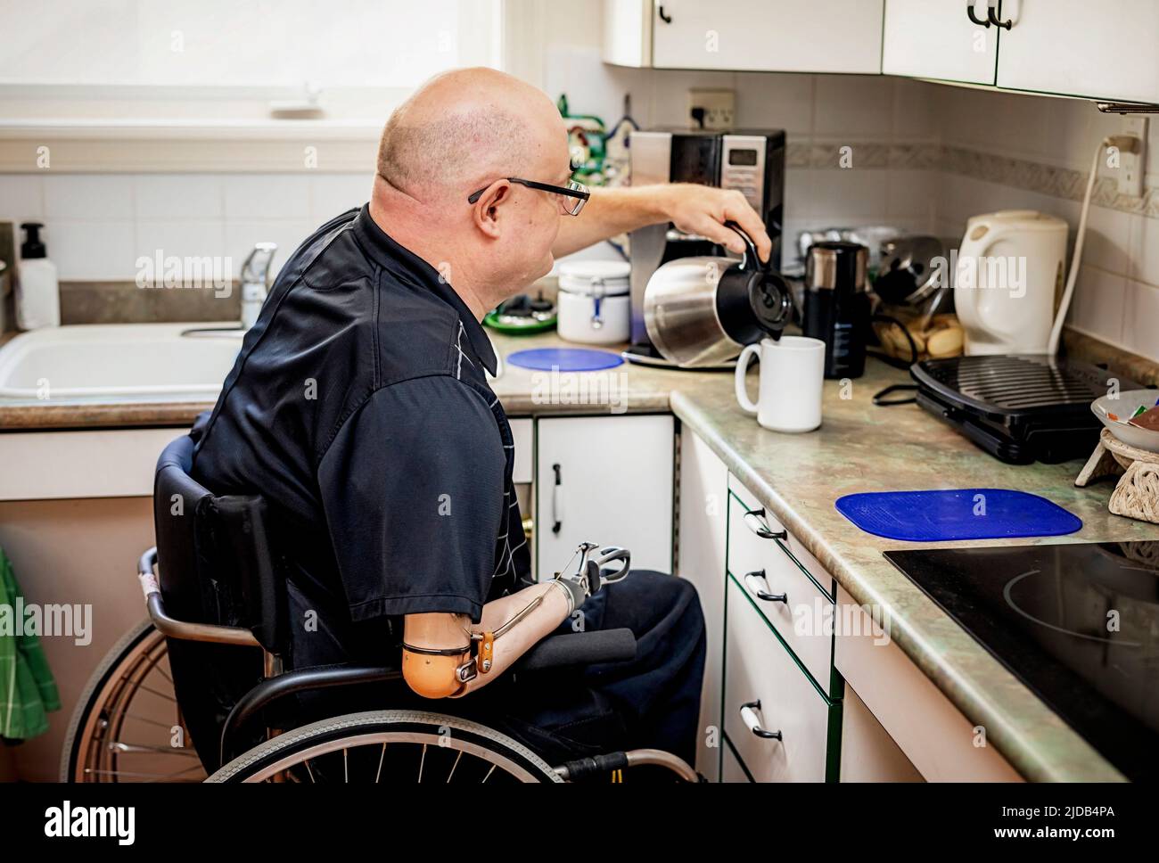 Homme avec des amputations de deux membres versant du café dans la cuisine à la maison; St. Albert, Alberta, Canada Banque D'Images