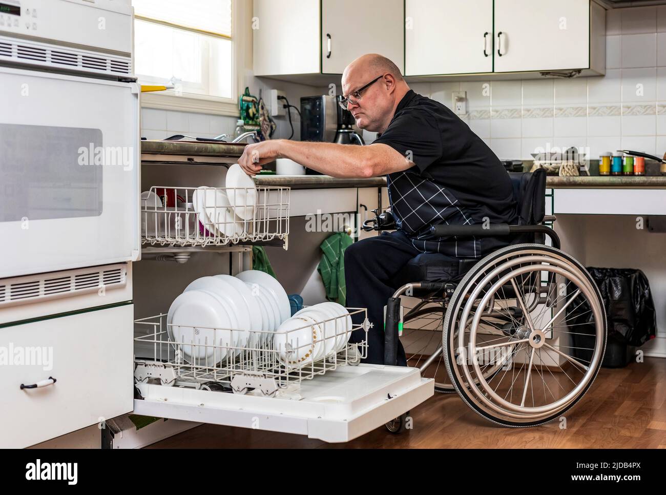 Homme avec des amputations de deux membres chargeant le lave-vaisselle dans la cuisine à la maison; St. Albert, Alberta, Canada Banque D'Images