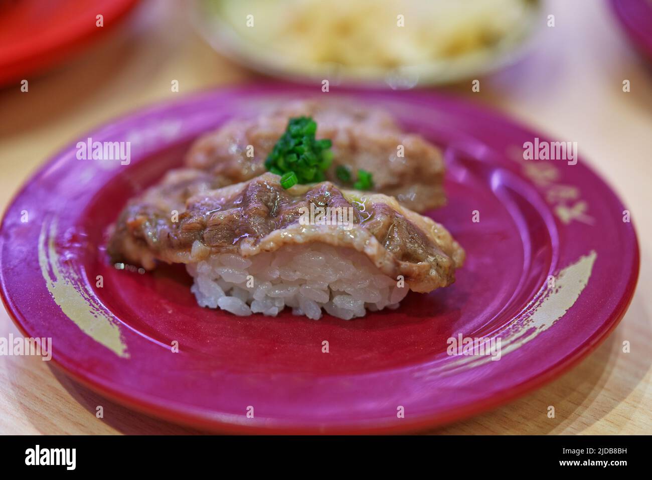 Gros plan des sushis de bœuf tranchés sur un plat rouge dans le restaurant sushi, griller le bœuf avec du sel sur le riz sushi, en ajoutant de l'oignon vert haché. Banque D'Images
