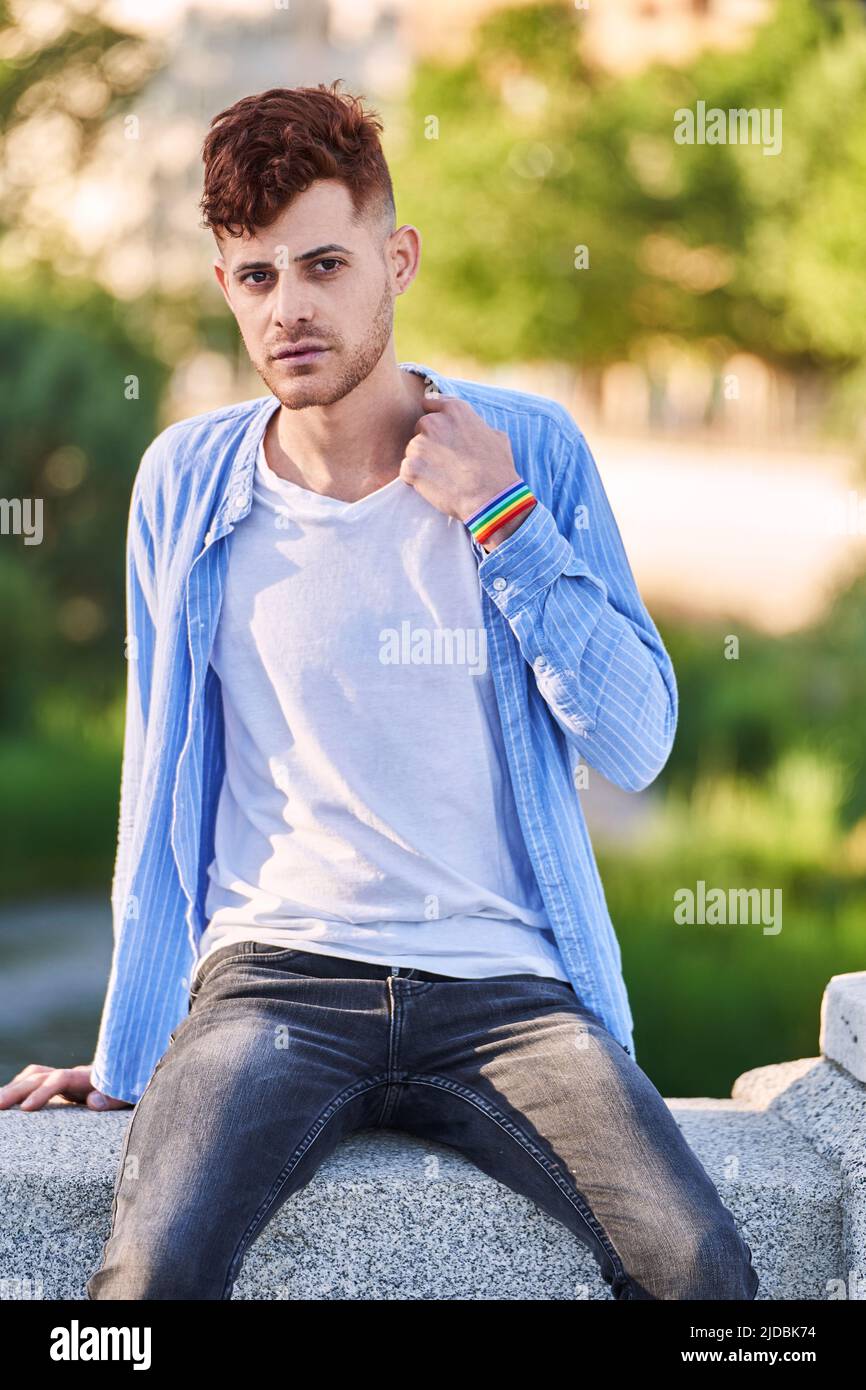 Jeune homme gay avec bracelet lgtb assis sur un mur de parc. Concept de LGBT, relation et égalité des droits. Banque D'Images