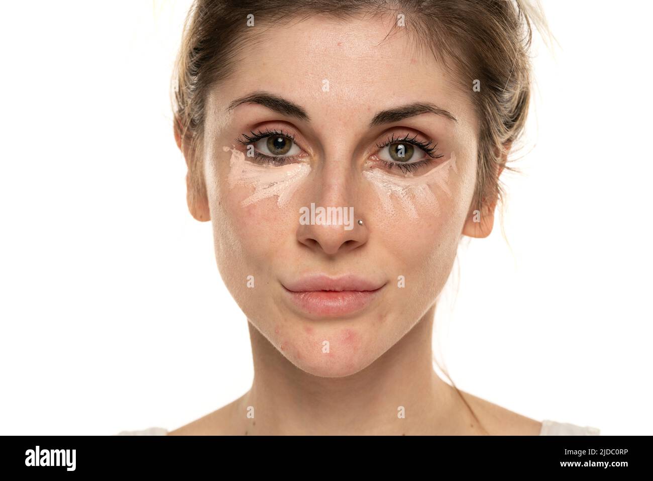 Jeune femme posant avec le correcteur sous ses yeux sur fond blanc. Banque D'Images