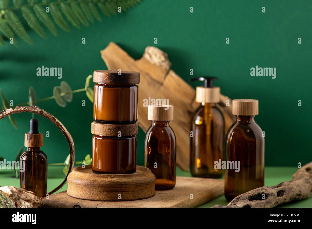 Récipients marron en verre pour cosmétiques avec couvercles en bois. Pot à crème, flacon compte-gouttes et lotion. Arrière-plan vert. Soins et beauté. Bouteilles. Concept écologique. Ensemble de cosmétiques. Pipette et distributeur. Banque D'Images