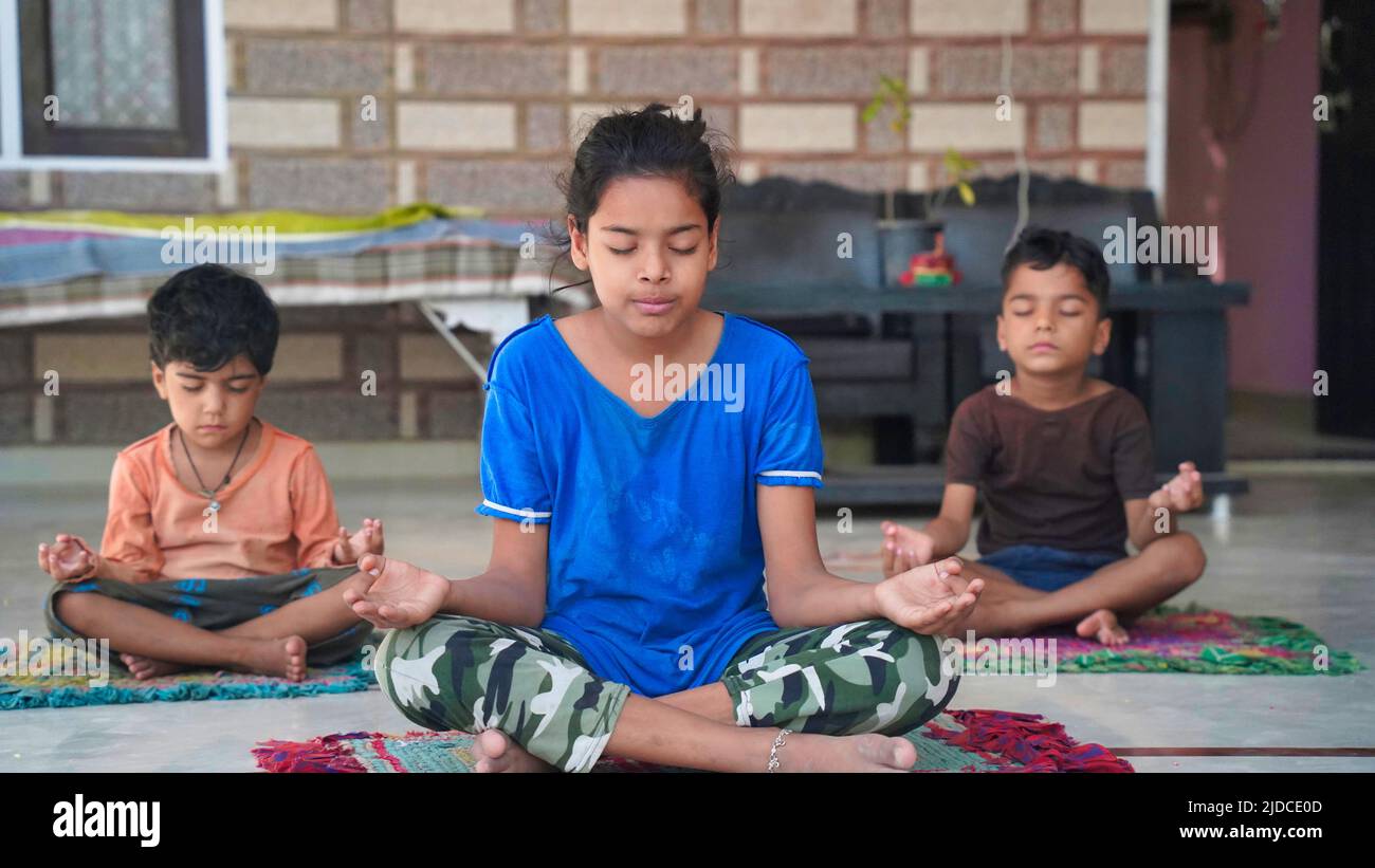 Trois petits enfants indiens faisant méditer l'asana de yoga sur tapis de rouleau avec les yeux fermés à la maison. Banque D'Images