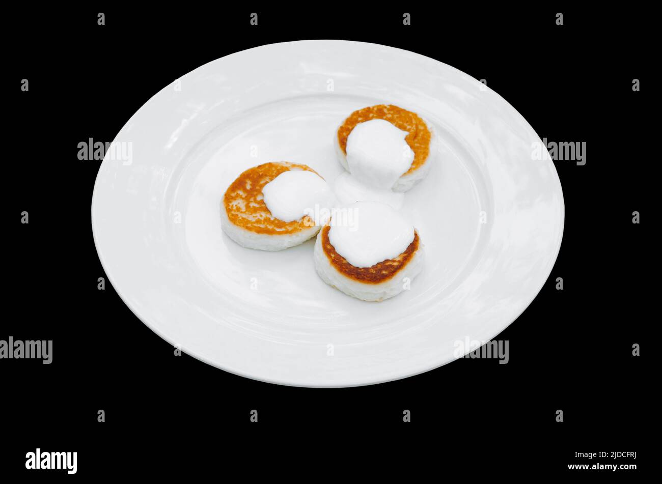 Beignets de fromage cottage Syrniki avec crème sure sur l'assiette. Arrière-plan noir isolé. Dessert caillé pour le petit déjeuner. Banque D'Images