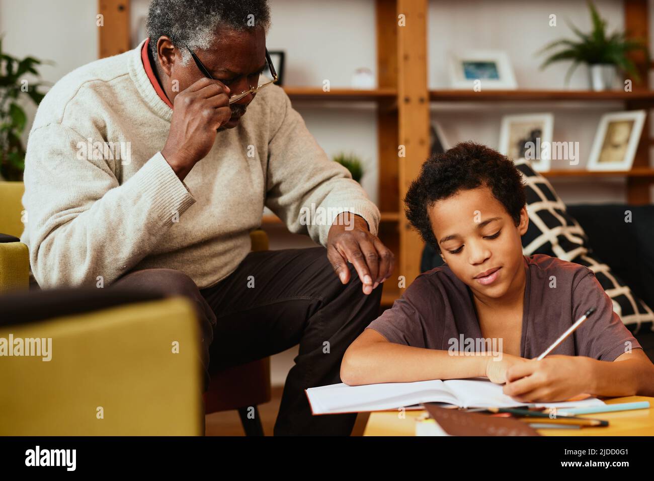 Un garçon africain intelligent qui fait ses devoirs de mathématiques avec un peu d'aide de son grand-père. Tutorat et éducation Banque D'Images