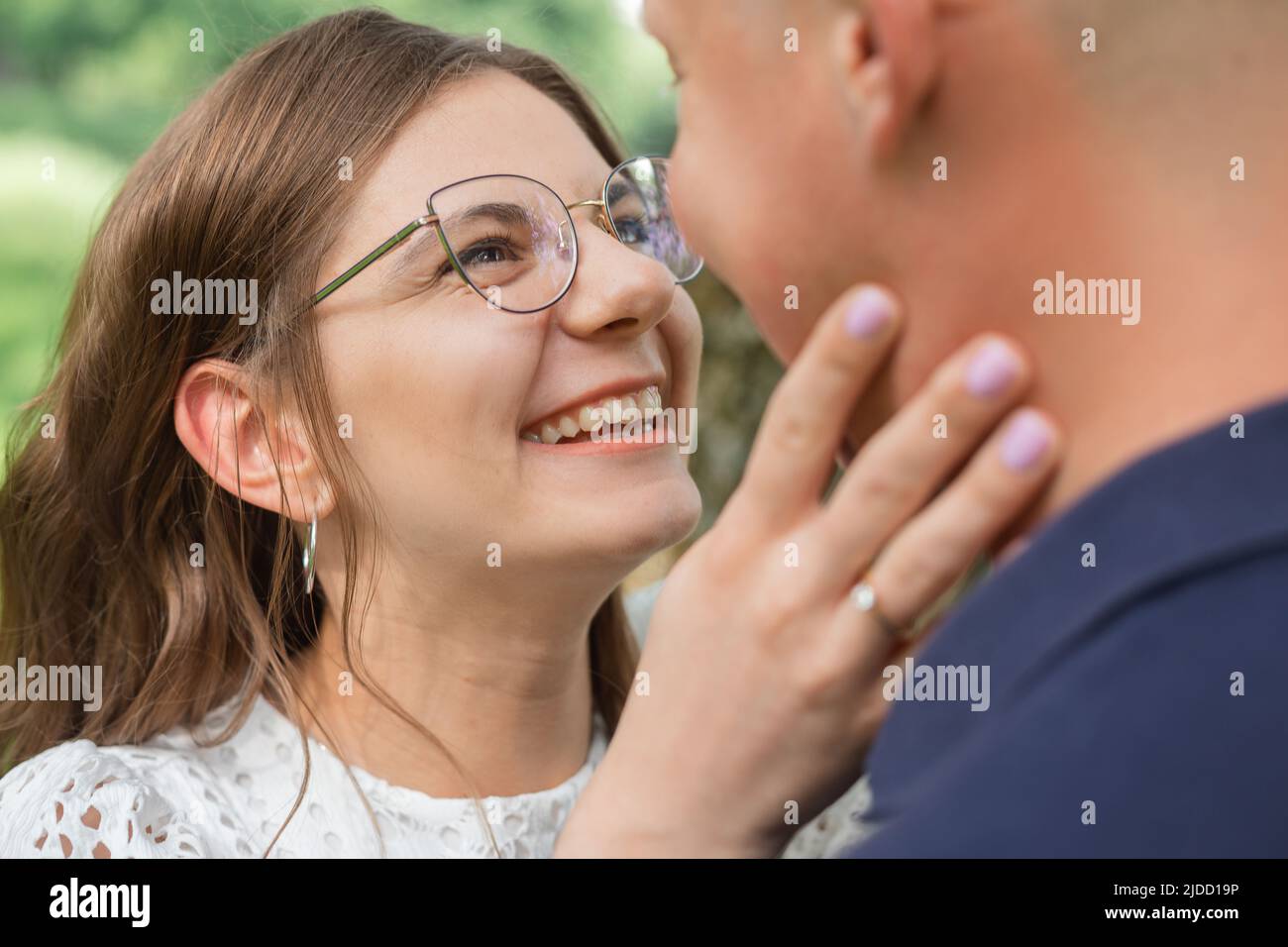 Gros plan portrait de belle femme avec des cheveux sombres dans les lunettes souriant et essayant de embrasser le petit ami dans le parc, datant Banque D'Images