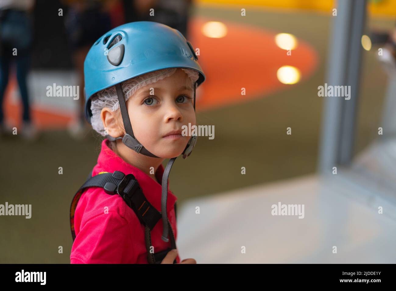 Jolie petite fille grimpeur dans un casque de protection bleu et équipement pour grimper debout dans le parc d'attractions du centre grimpeur pour les enfants. clim femelle caucasien Banque D'Images