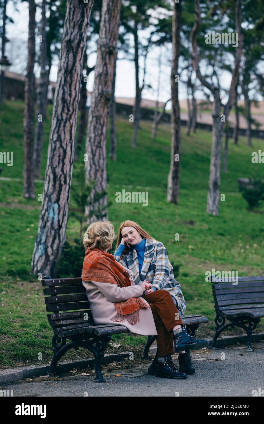 Une grand-mère rit et s'amuse avec sa petite-fille adolescente lorsqu'elle est assise sur le banc du parc. Banque D'Images