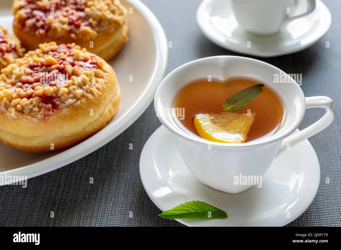 Beignets sucrés sur les assiettes et les tasses avec thé à la menthe sur la table grise. Petit déjeuner savoureux. Banque D'Images