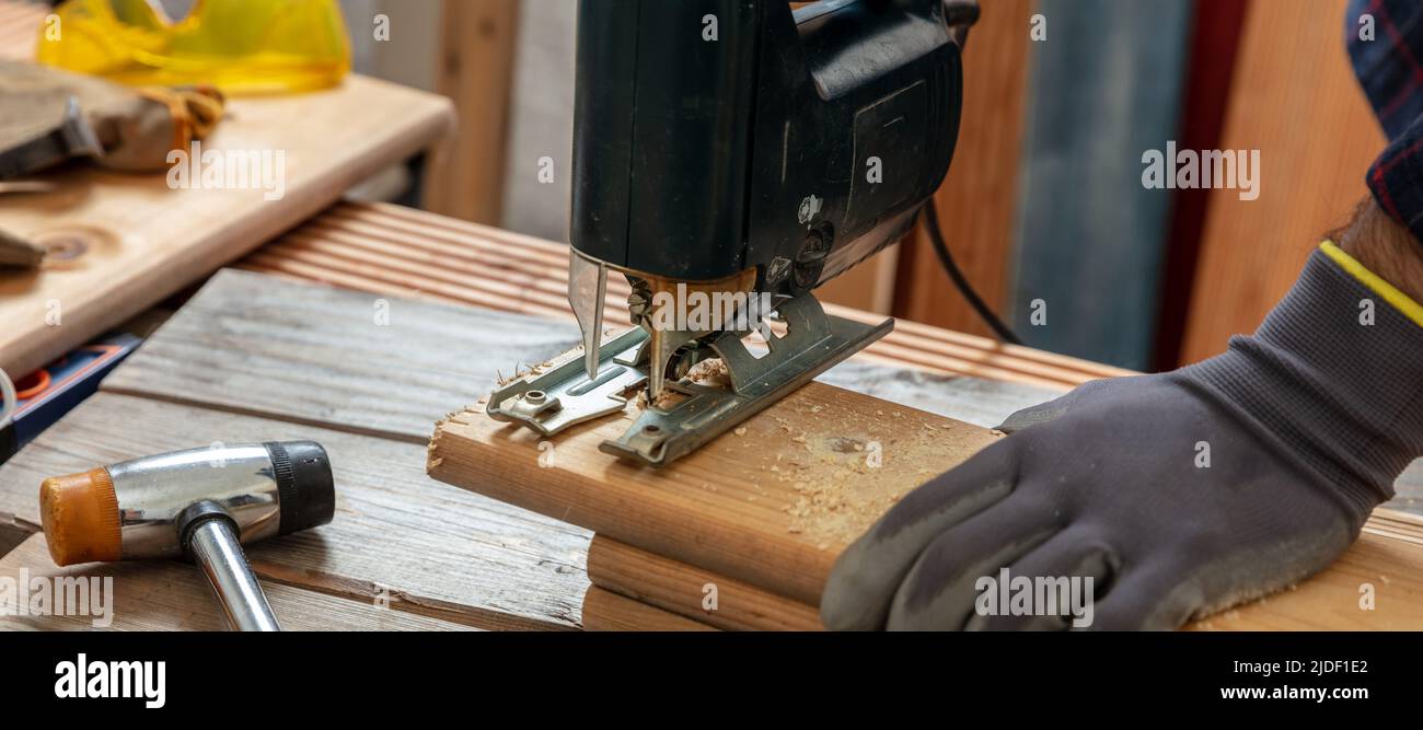 Scie électrique, menuisier ganté coupe main du bois avec une scie sauteuse électrique. Industrie de la construction, table de travail vue rapprochée Banque D'Images