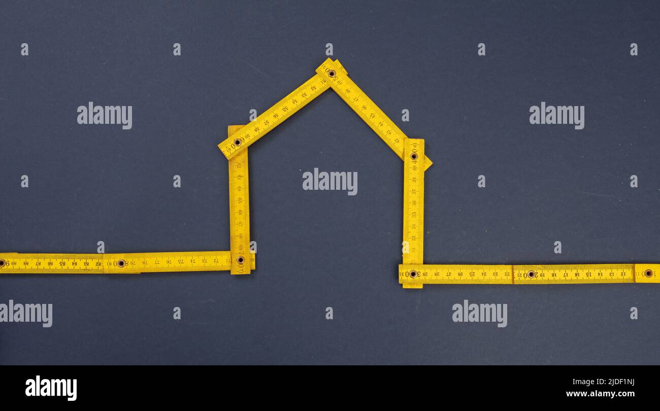 Maison forme jaune mesure en bois sur fond bleu. Règle pliante pour architecte, mécanicien pour construction, entretien de maison, rénovation, répare Banque D'Images