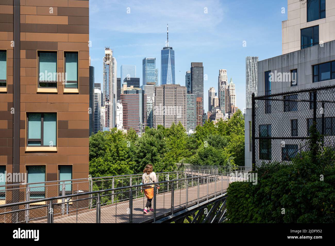 Femme marchant sur la passerelle piétonne Squibb Park Bridge avec les immeubles de Lower Manhattan en hauteur en arrière-plan à New York City, États-Unis Banque D'Images