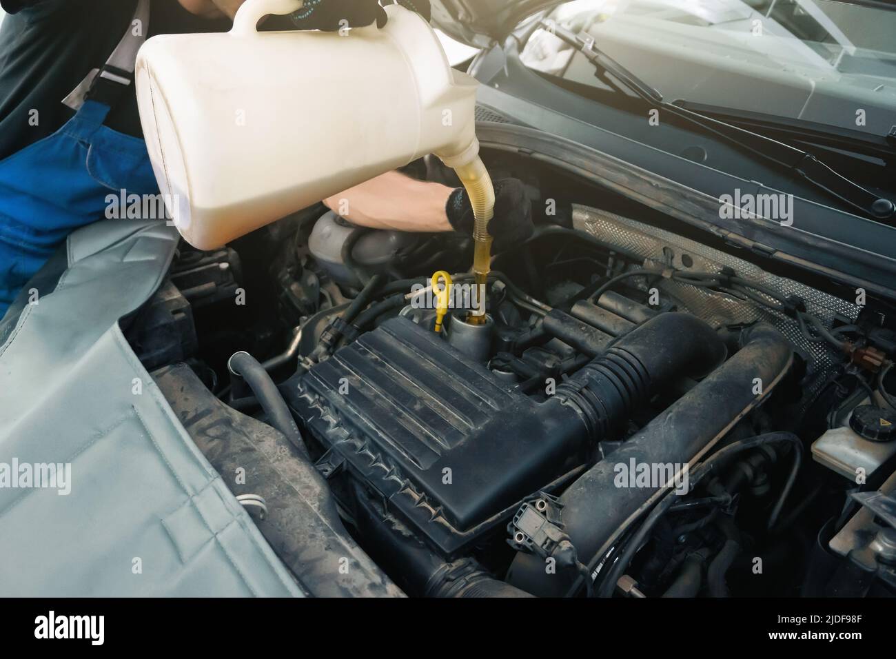 Un technicien de maintenance verse de l'huile moteur dans le moteur dans le garage d'entretien de la voiture, en gros plan. Banque D'Images