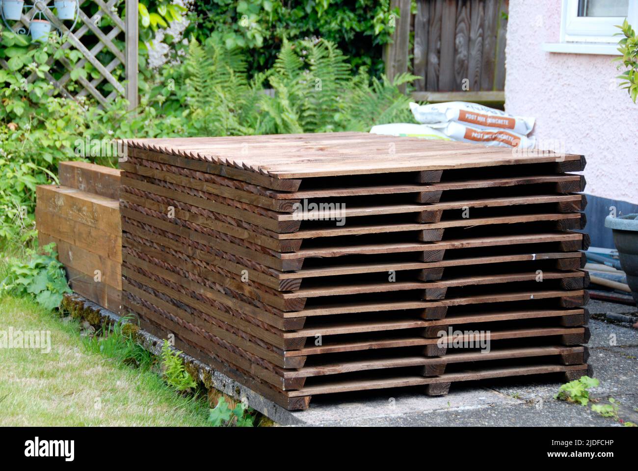 Pile de panneaux de clôture en bois, poteaux, planches de gravier et mélange de ciment, entreposée sur le patio prêt pour le remplacement de l'ancienne clôture de jardin domestique Banque D'Images
