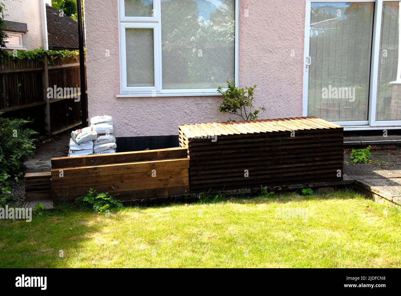 Pile de panneaux de clôture en bois, poteaux, planches de gravier et mélange de ciment, entreposée sur le patio prêt pour le remplacement de l'ancienne clôture de jardin domestique Banque D'Images