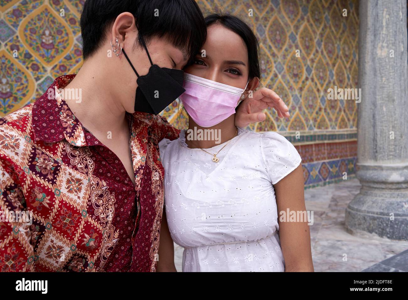Couple multiculturel et transgenre embrassant tendinement devant un temple bouddhiste Banque D'Images