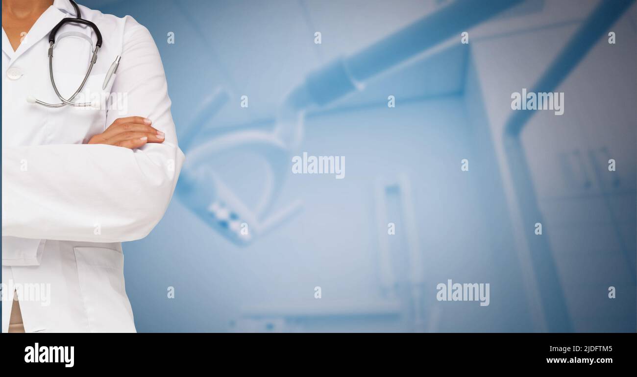 Milieu de la section de la femme mixte-race médecin avec les bras croisés contre l'hôpital en arrière-plan Banque D'Images