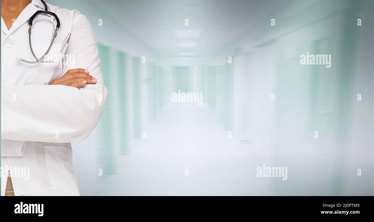 Milieu de la section de la femme mixte-race médecin avec les bras croisés contre l'hôpital en arrière-plan Banque D'Images