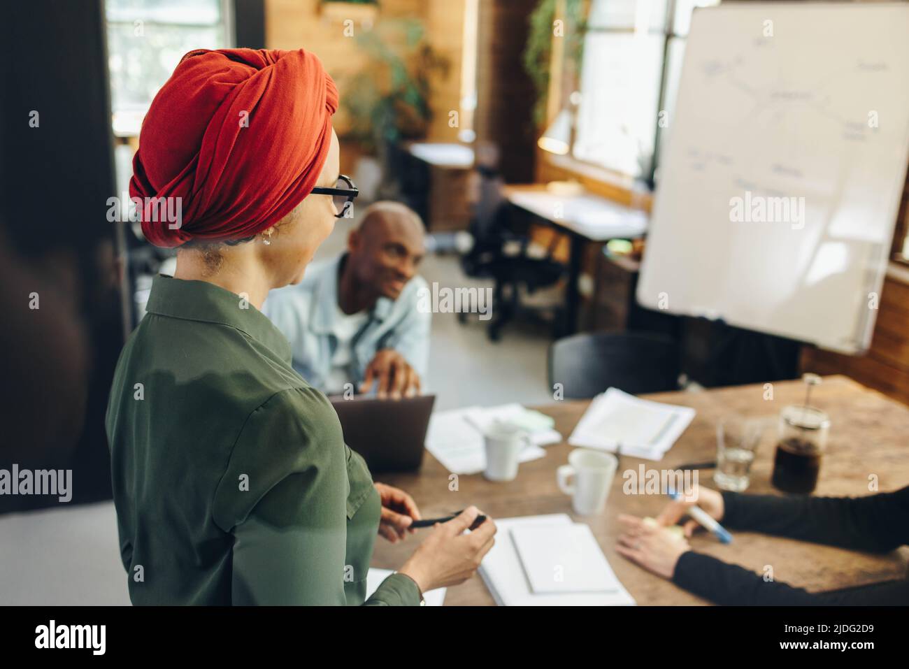 Chef d'équipe musulman ayant une réunion avec ses collègues d'affaires dans une salle de réunion moderne. Bonne femme d'affaires ethnique portant un foulard dans un multiticultu Banque D'Images