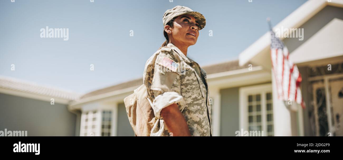 Femme courageuse soldat regardant loin avec soin tout en se tenant à l'extérieur de sa maison avec son sac. Un militaire américain rentrent chez lui après le début du service Banque D'Images