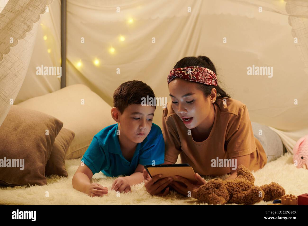 Mère lisant un livre électronique à son fils lorsqu'ils sont couchés sur le sol dans une grande tente Banque D'Images