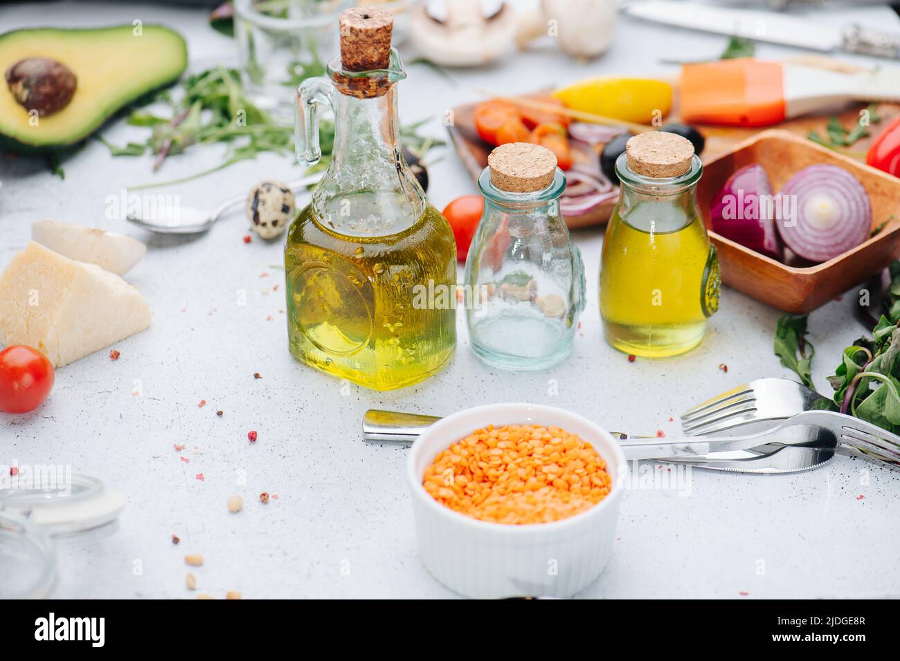 Graines dans une tasse devant les bouteilles d'huile et autres ingrédients de cuisson sur une table. Olives, oignons, légumes verts et tomates. Banque D'Images