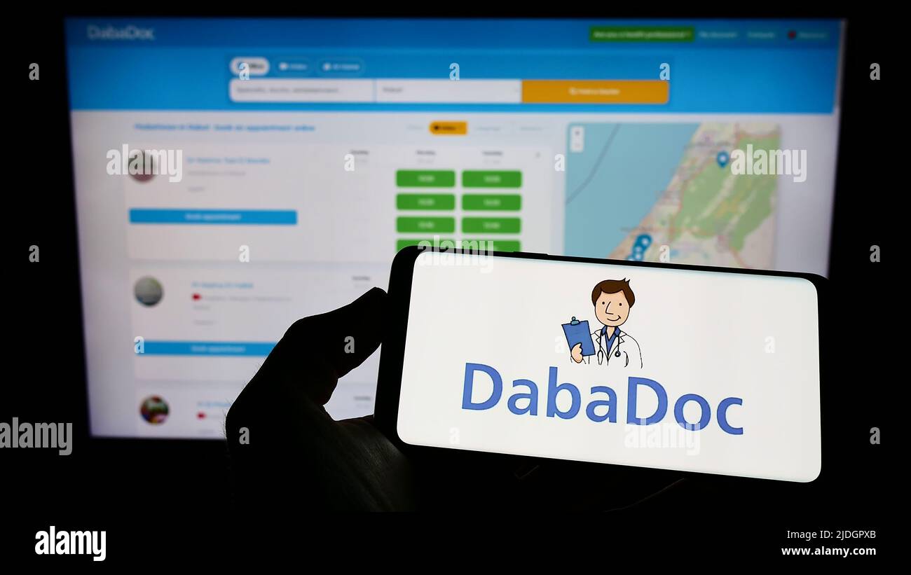 Personne tenant un téléphone portable avec le logo de la société marocaine de soins de santé DabaDoc à l'écran en face de la page web d'affaires. Mise au point sur l'affichage du téléphone. Banque D'Images