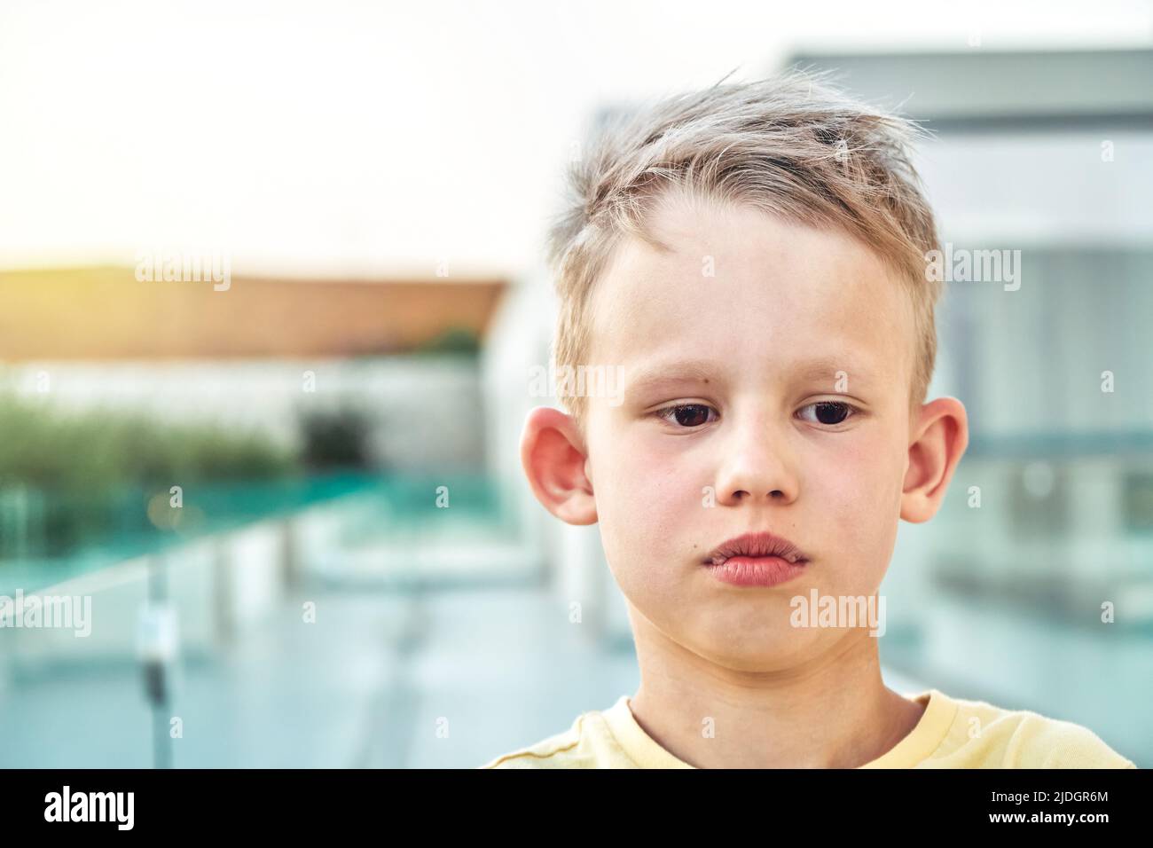 Portrait d'un élève triste avec des cheveux blonds sur un arrière-plan flou. Un petit garçon mignon a l'air de se tenir debout contre le territoire de l'hôtel à proximité de la station Banque D'Images