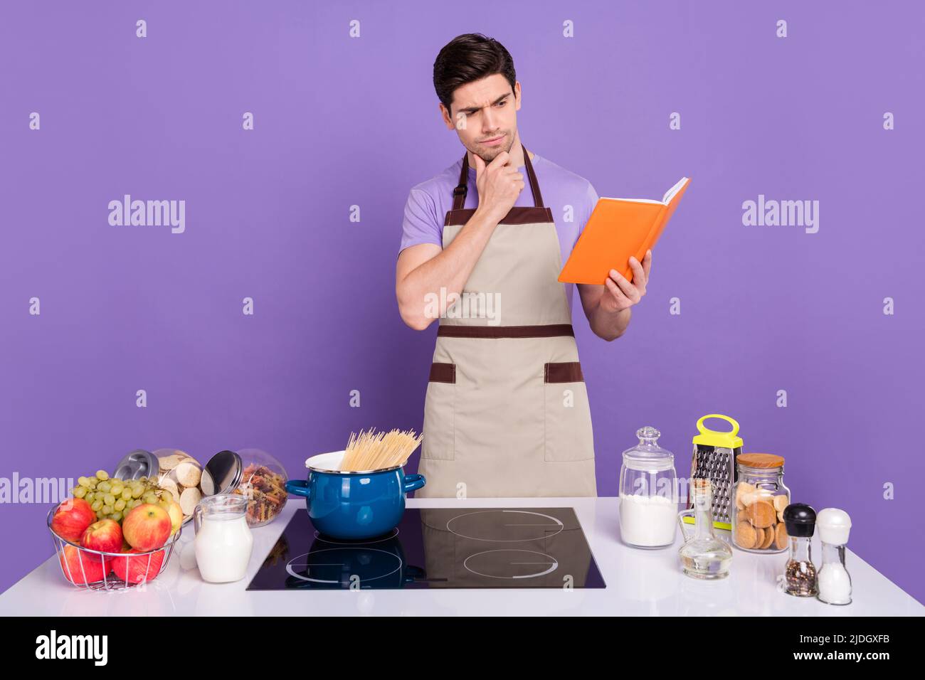 Photo de l'incertain ponder mari porter des tabliers gris lecture lourde long nouveau souper recette isolé couleur violet fond Banque D'Images