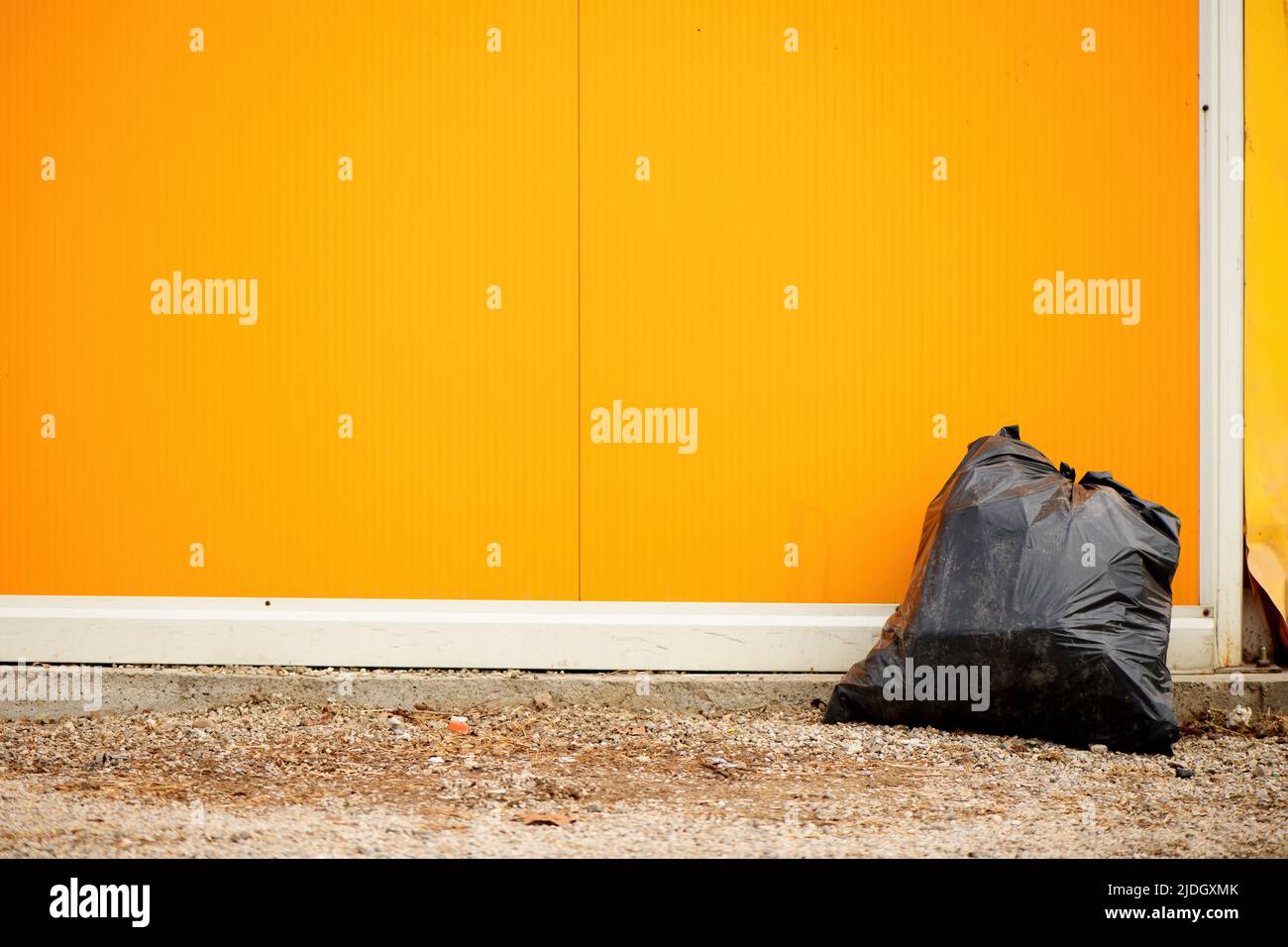 Sac poubelle en plastique noir dans la rue contre le mur jaune Banque D'Images